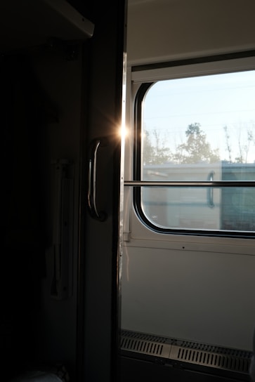 A cozy train compartment window view showing passing green fields under a soft morning light.