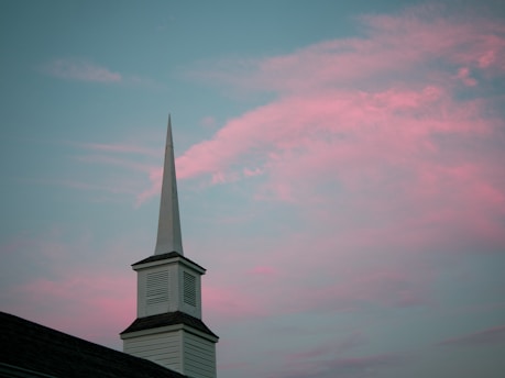 A serene church steeple silhouetted against a soft sunrise sky.