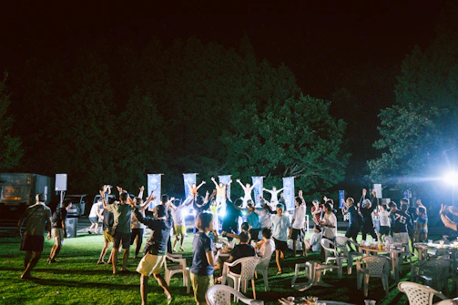 Wide shot of an outdoor night party with glowing decorations and lively crowd.