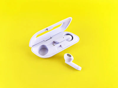 An electric blue wireless earbud set resting on a sunny yellow surface, emphasizing its compact and trendy look.