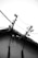 A rooftop with several electrical insulators and wires is silhouetted against a bright white sky. The stark contrast emphasizes the angular lines of the wires and insulators, giving it a geometric appearance. The texture of the roof and the materials used are evident in the image's details.