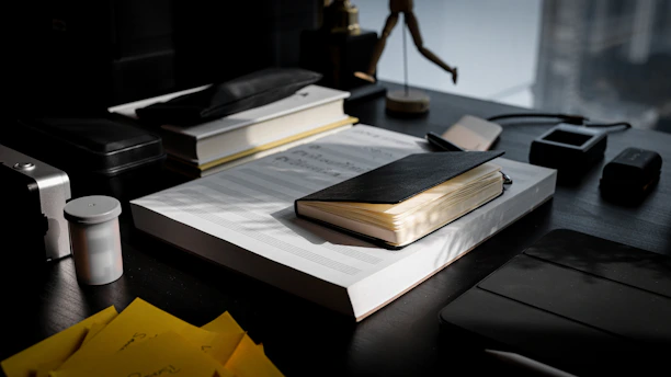 Close-up of a sleek black leather-bound portfolio resting on a dark wood desk under soft, muted lighting.