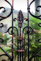 Close-up of a black wrought iron gate opening to a beige stucco house.