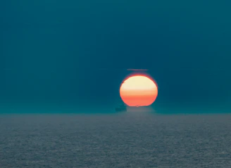 A warm, inviting orange sun rising over a calm blue horizon, symbolizing awakening and hope.
