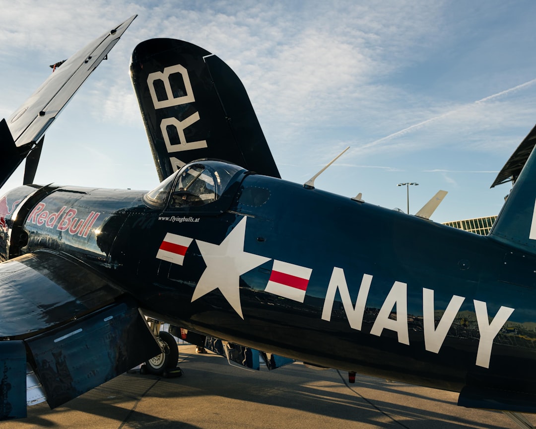 a navy plane parked on the tarmac at an airport, RedBull Navy Vought F4U stands with wings folded at Zurich airport