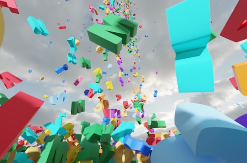 A vibrant array of colorful 3D letters and numbers is suspended mid-air against a cloudy sky backdrop. The characters appear to be in various fonts and sizes, contributing to a chaotic yet lively scene. There is a sense of movement as if the characters are either falling or floating upward.