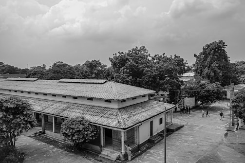 A black-and-white photo of the original school building from 1954 surrounded by village scenery.