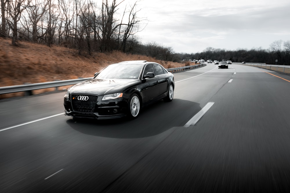 a black car driving down a highway next to a forest