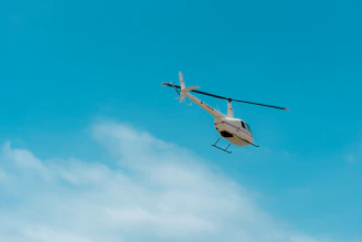 A helicopter soaring above the Himalayan mountains near Kedarnath under a clear blue sky.