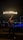 A fire performer is standing outdoors at night, skillfully manipulating a flaming baton. The word 'AFRICANFIREMAN' is emblazoned in flames above, illuminating the dark surroundings. The setting appears to be near a poolside with loungers and subtle lighting, creating a vibrant atmosphere.