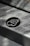 A pattern of stylized 'B' letters is printed on a smooth metallic or paper surface. A large black circle in the center highlights one of the 'B' letters, with smaller ones scattered around it. There's a message at the top regarding saving trees, indicating an environmentally conscious theme.