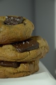 Three stacked chocolate chip cookies with large chunks of chocolate on top, sprinkled with sea salt, resting on a light surface.