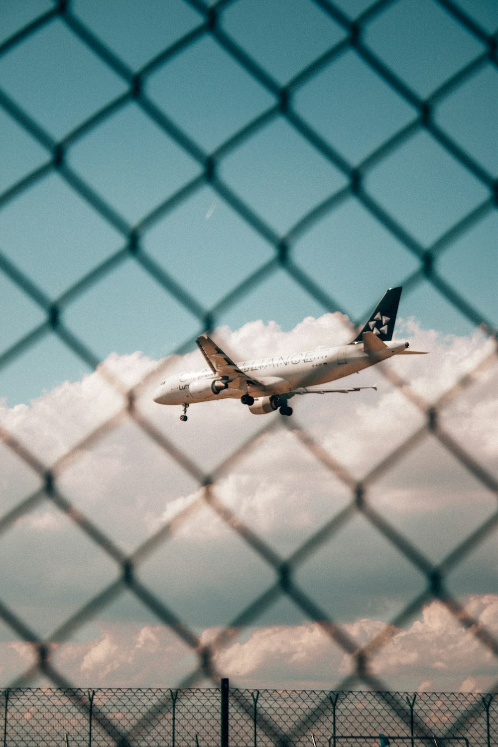 Un avion vole dans le ciel derrière une clôture à mailles de chaîne