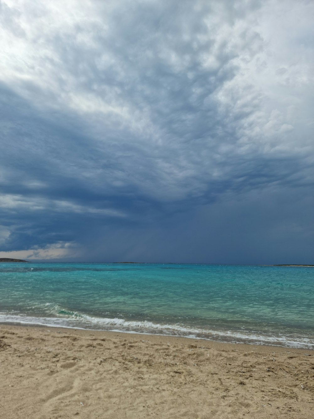 a sandy beach next to the ocean under a cloudy sky