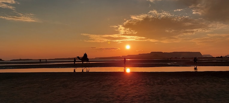 A serene desert sunset over Dubai's skyline with a silhouette of a traveler enjoying the view.