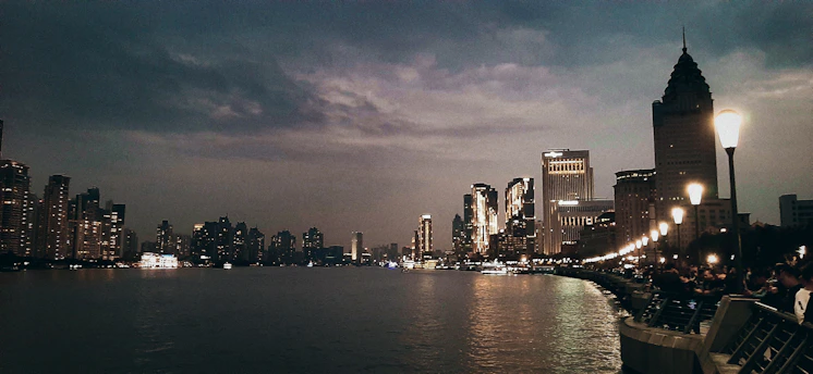 A vibrant city skyline at dusk with travelers walking and working on laptops outdoors.