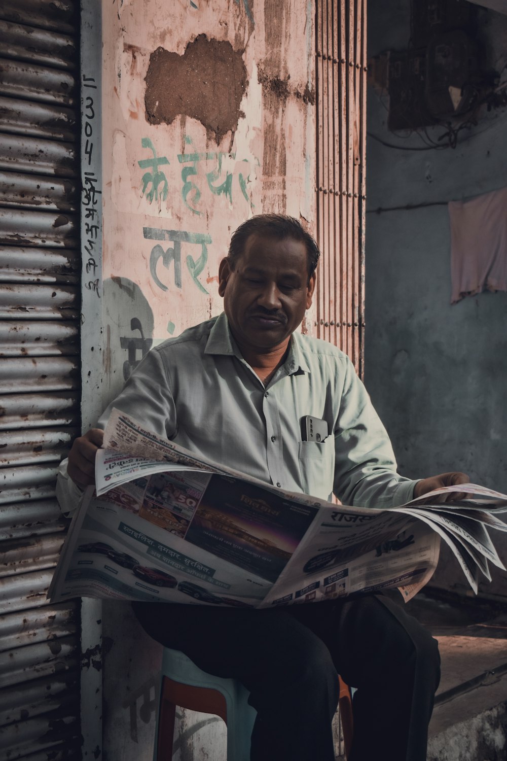 a man sitting on a stool reading a newspaper