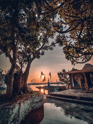 A serene riverside scene at dusk with a traditional Ganga aarti lamp glowing softly against a backdrop of maroon and saffron hues.