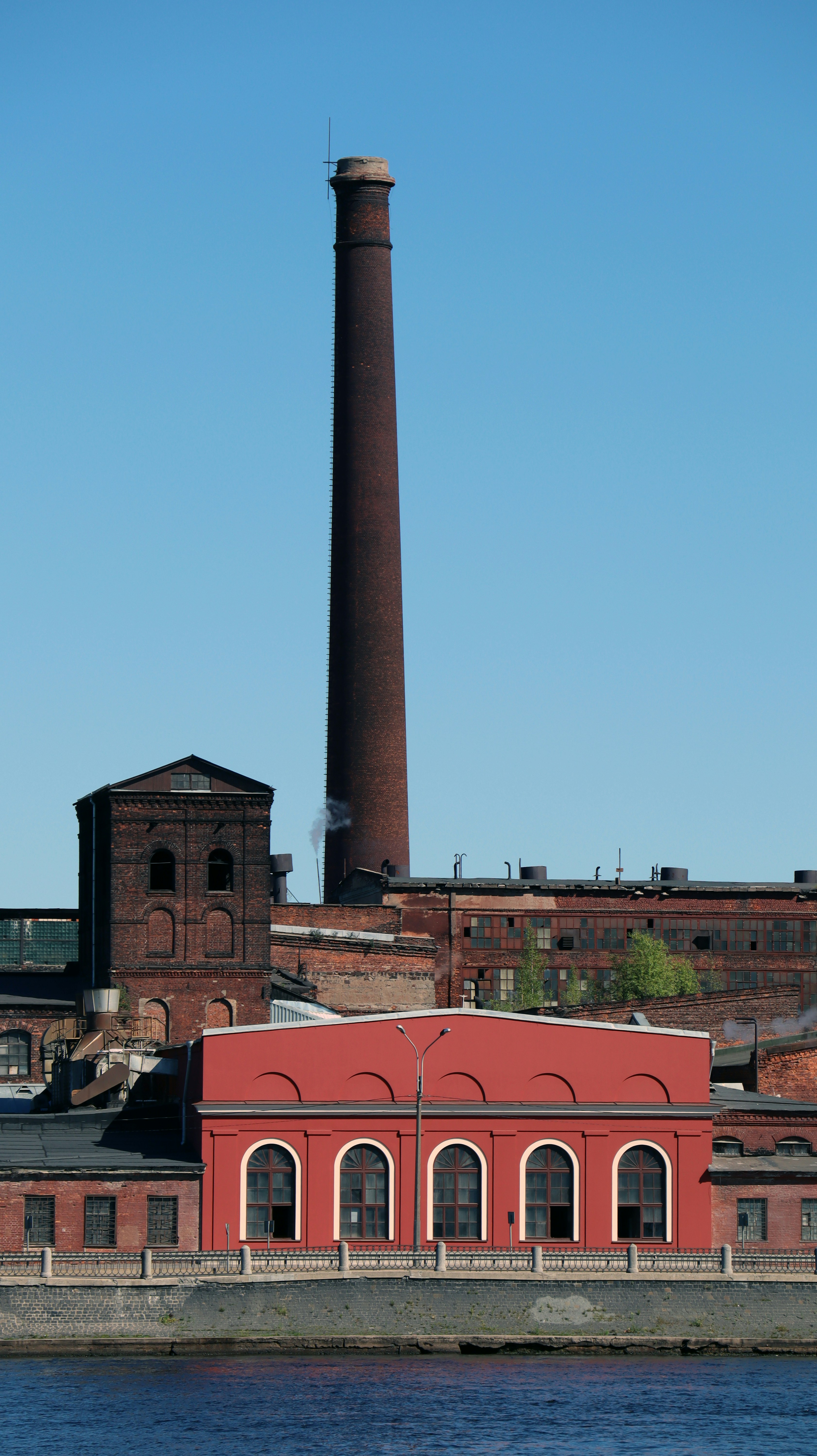 A red brick building with a tall chimney next to a body of water photo ...