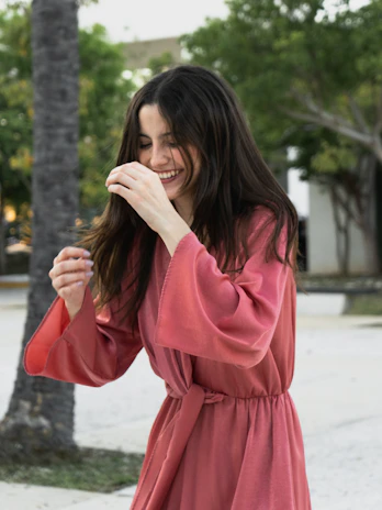 A joyful woman wearing a flowing dress with pockets, holding her phone and keys comfortably.