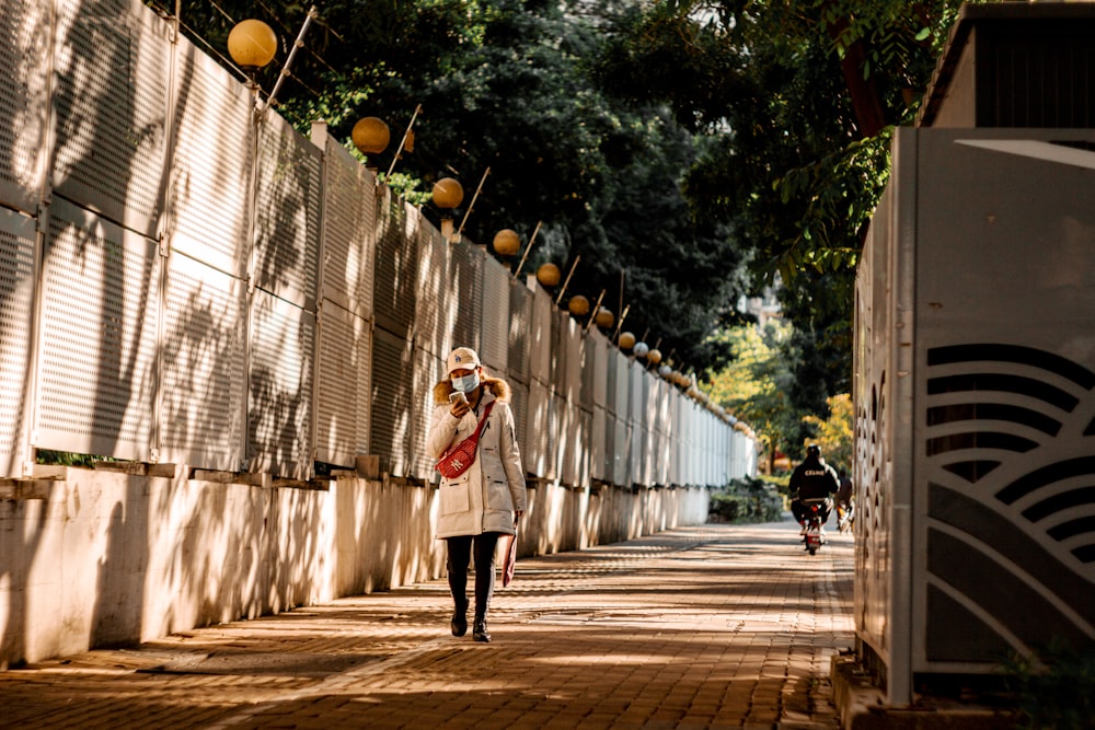 a woman walking down a sidewalk next to a fence