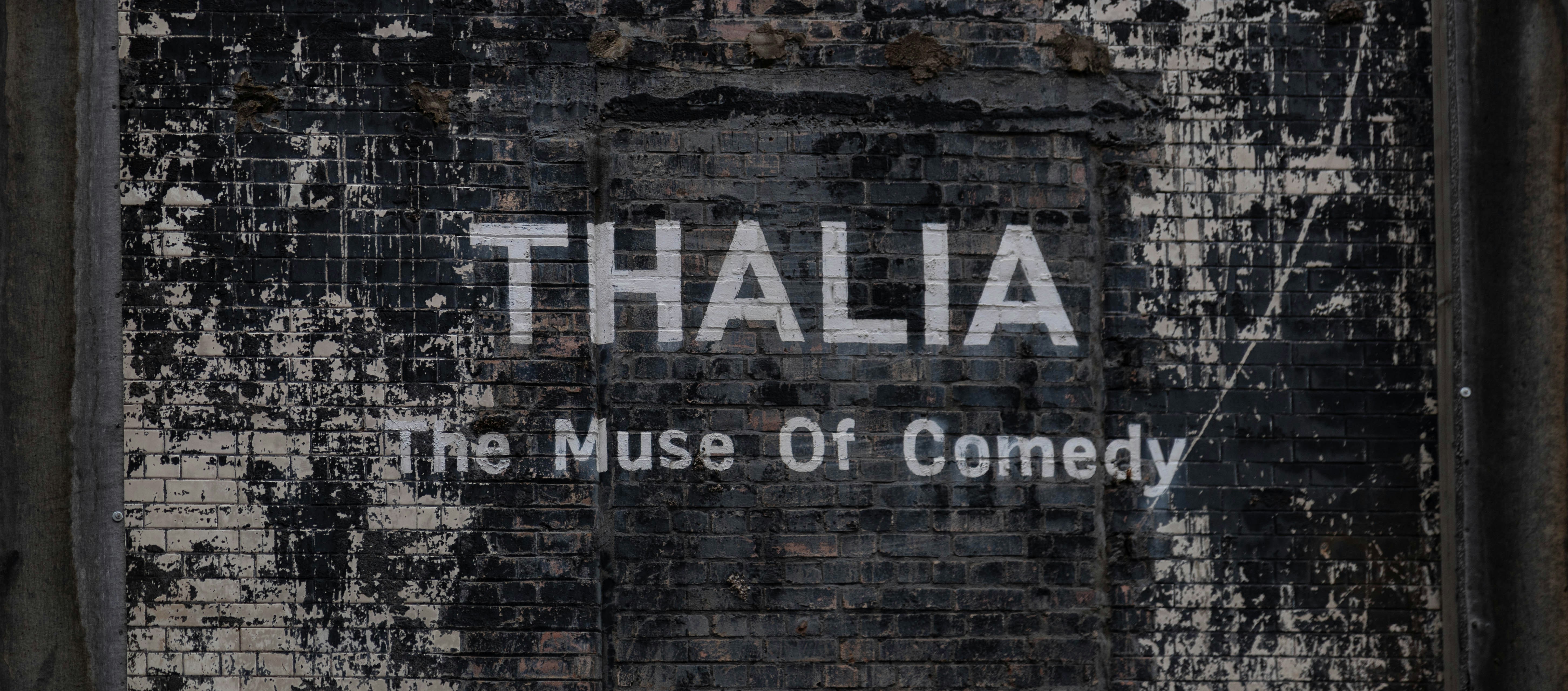 a sign on the side of a building that says thalia the museum of comedy, 
