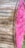 A large wooden spool with a vibrant pink end cap and industrial text stenciled in black. The spool is oriented diagonally, highlighting the contrast between the natural wooden texture and the bright pink color. Some greenery is visible at the bottom right edge of the image.