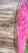 A large wooden spool with a vibrant pink end cap and industrial text stenciled in black. The spool is oriented diagonally, highlighting the contrast between the natural wooden texture and the bright pink color. Some greenery is visible at the bottom right edge of the image.