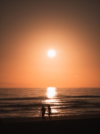 two people walking on the beach at sunset