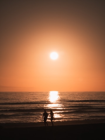 two people walking on the beach at sunset