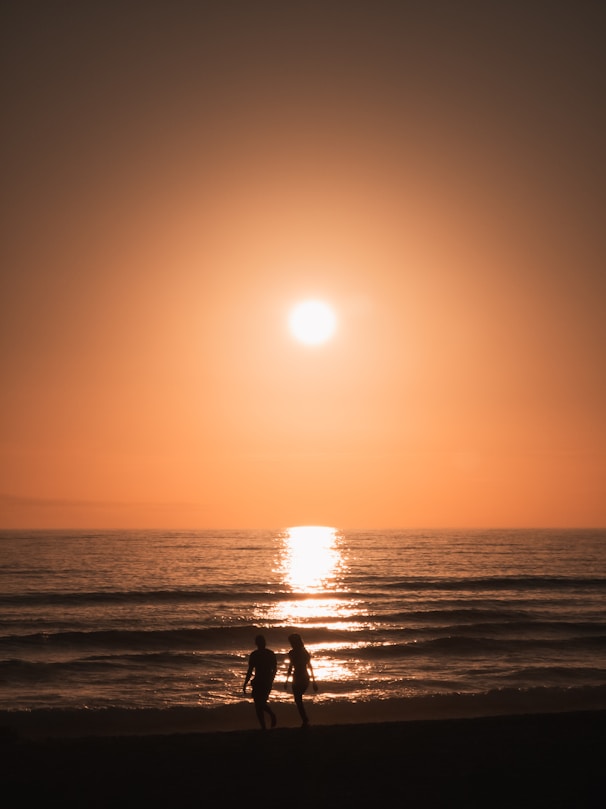 two people walking on the beach at sunset