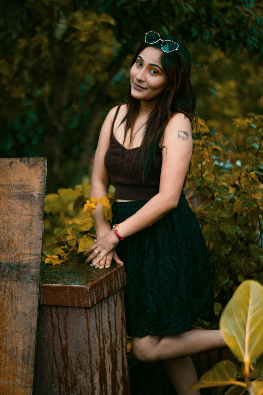 a woman in a black dress and sunglasses leaning on a wooden post