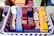 A basket containing neatly arranged stacks of colorful ceramic tiles in various shades such as blue, red, yellow, and white, with some featuring intricate patterns. The basket itself has a purple and white woven design.