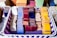 A basket containing neatly arranged stacks of colorful ceramic tiles in various shades such as blue, red, yellow, and white, with some featuring intricate patterns. The basket itself has a purple and white woven design.