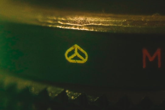 A close-up shot features a symbolic yellow icon resembling a triangular peace sign or a camera dial marking against a dark, textured background. Beside it, the letter 'M' is visible in red, suggesting a camera or photographic equipment setting.
