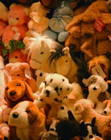 A variety of plush stuffed animals, including dogs, horses, and bears, are piled together in different colors such as brown, white, and pink. Some of these toys have tags attached to them, indicating they are from a store or collection.