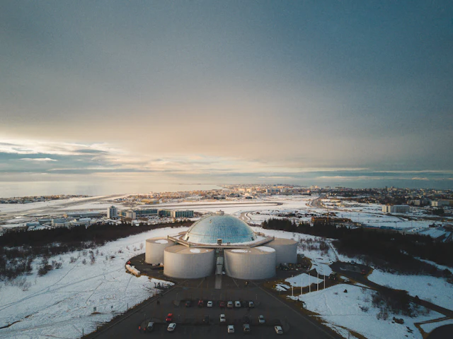 Aerial view of Perlan's glass dome on its cylindrical tanks above Reykjavik at sunset.