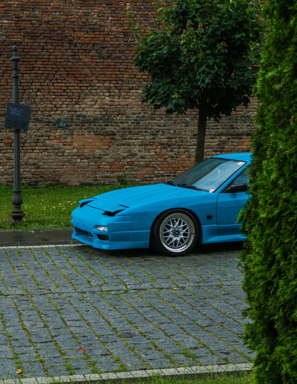 a blue sports car parked in front of a brick wall