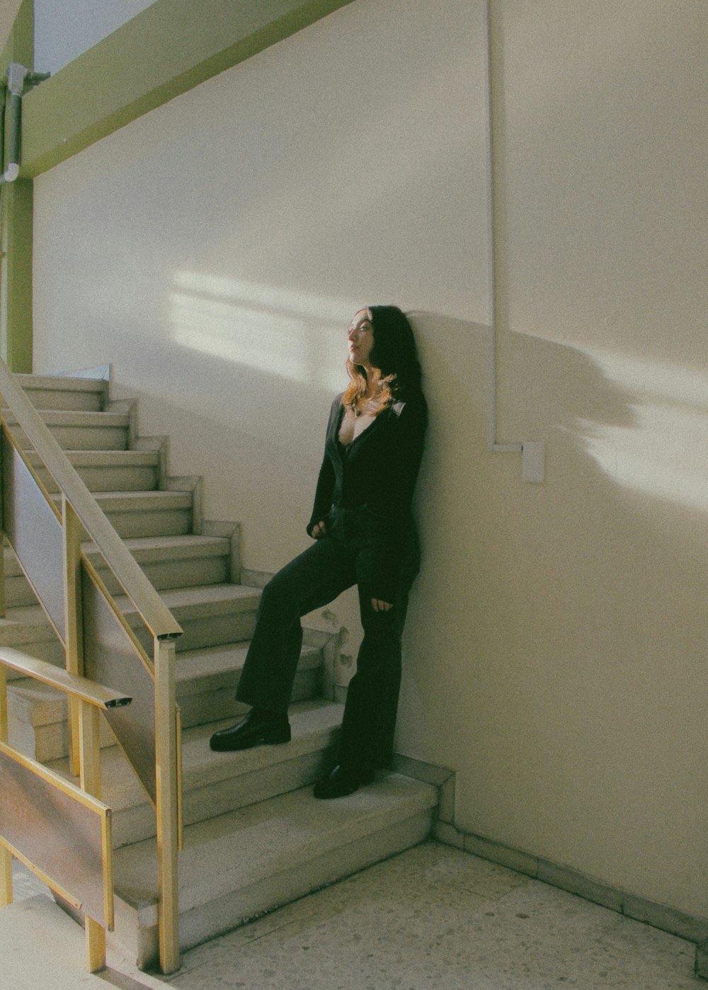 a woman leaning against a wall next to a stair case