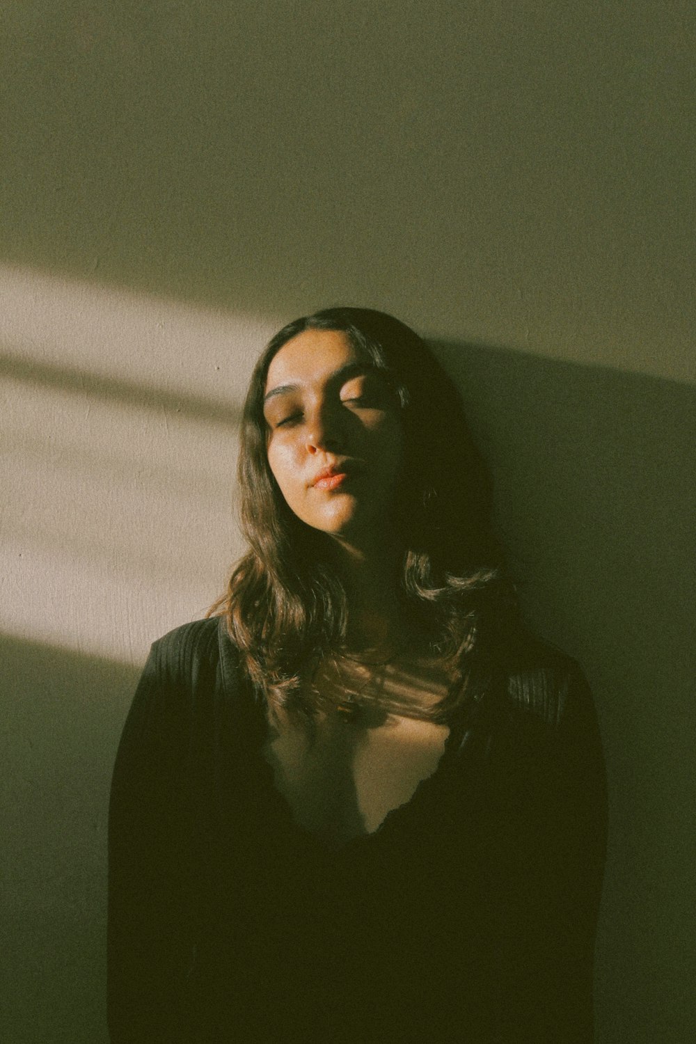 a woman standing in front of a wall with her eyes closed