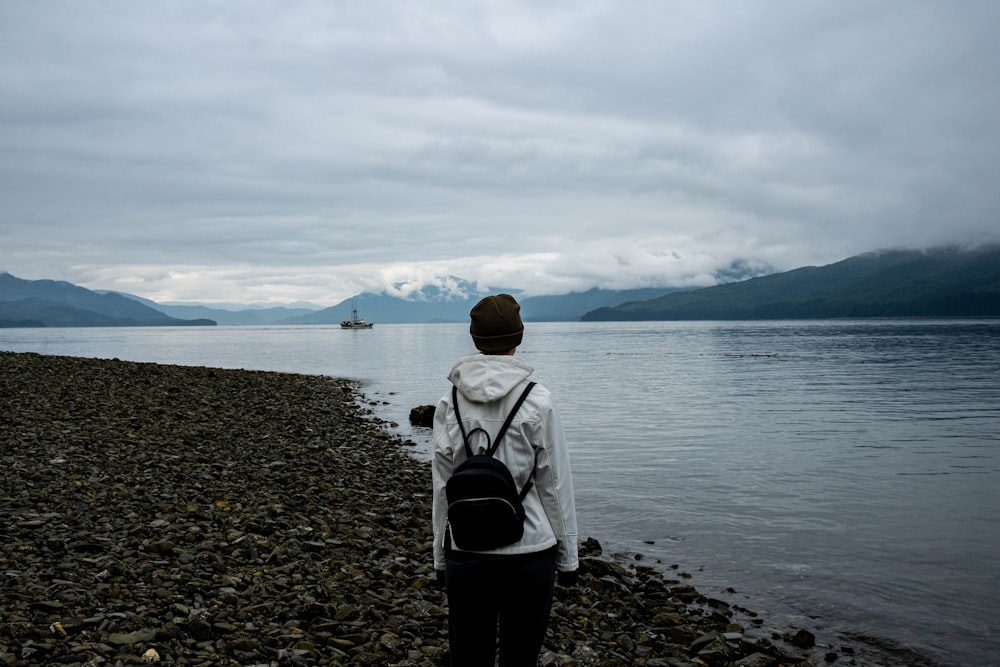 a person standing on a rocky beach with a backpack