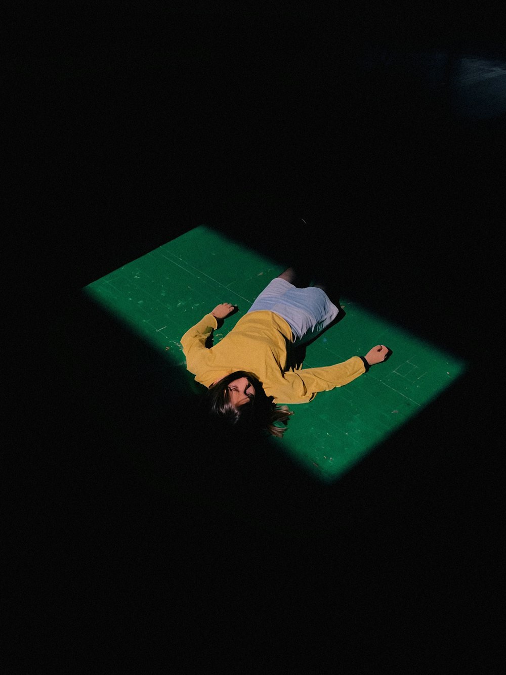 uma pessoa deitada em um tapete verde no escuro