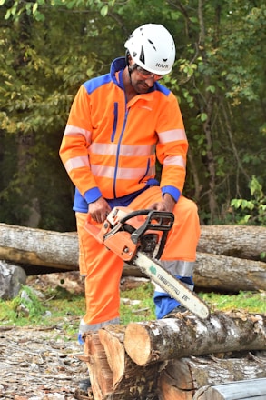 Technician in safety gear operating a chainsaw in a dense forest.