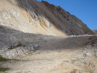Paysage montagneux avec un sentier sinueux sous un ciel bleu clair.