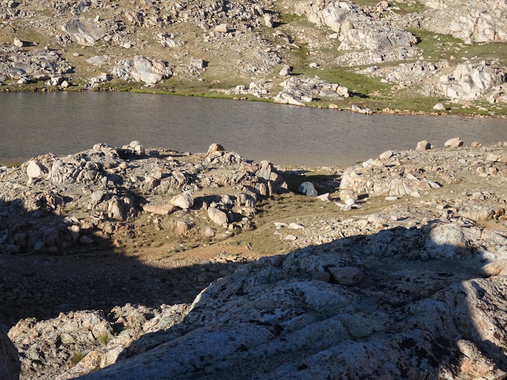 a man standing on top of a rocky hill next to a lake