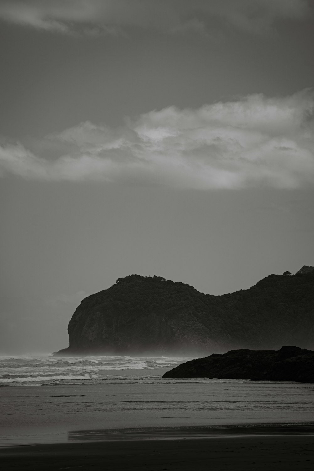 a black and white photo of a beach and a rock