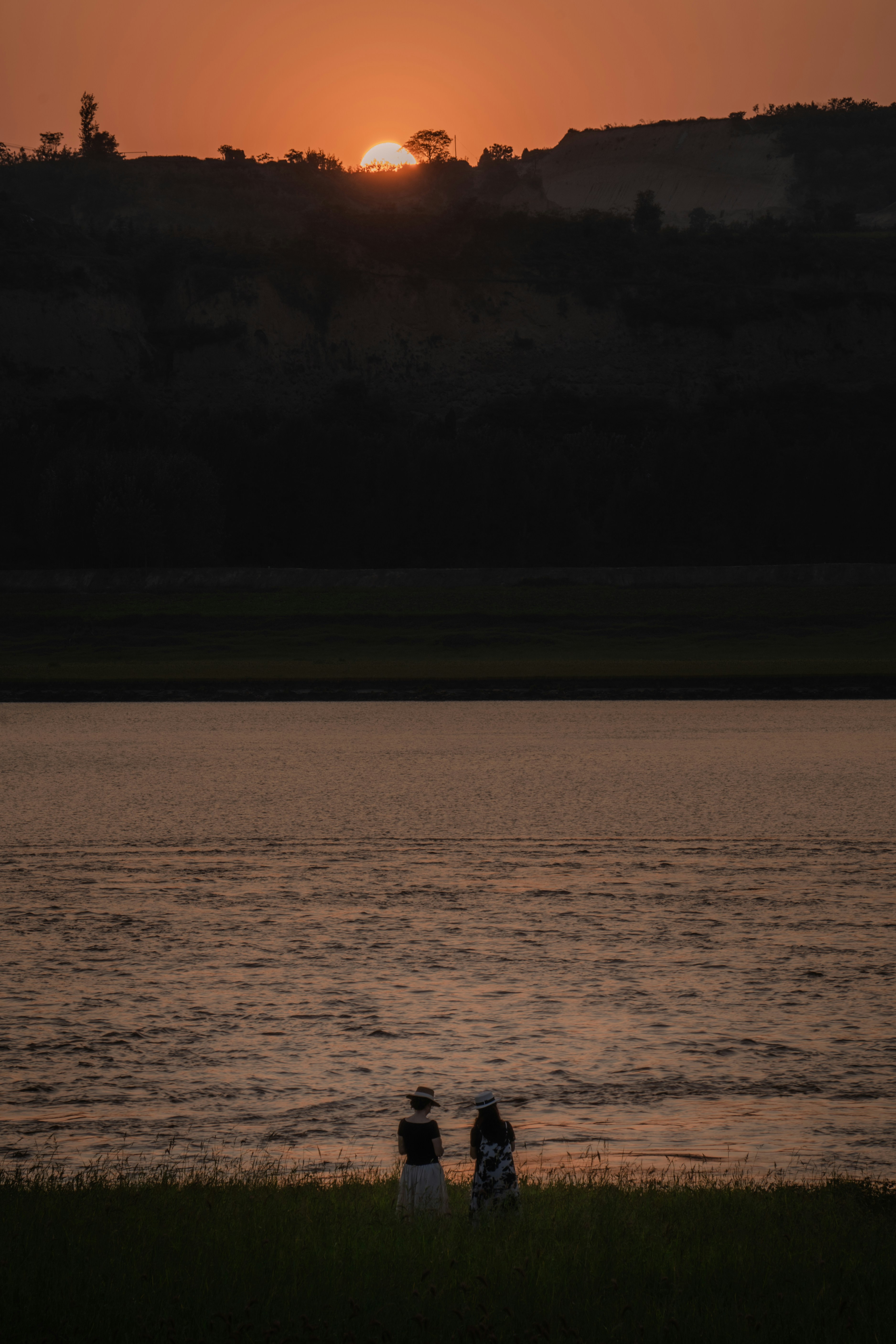 A couple of people sitting next to a body of water photo – Free Henan ...