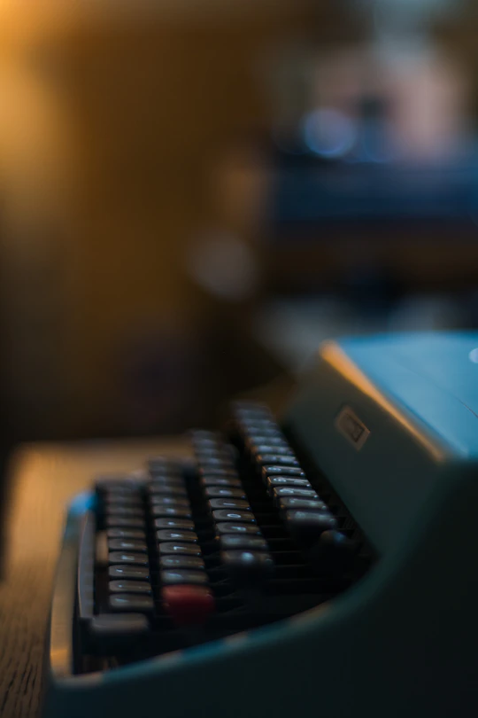 A close-up of a vintage typewriter with gold accents, softly lit against an off-white background.