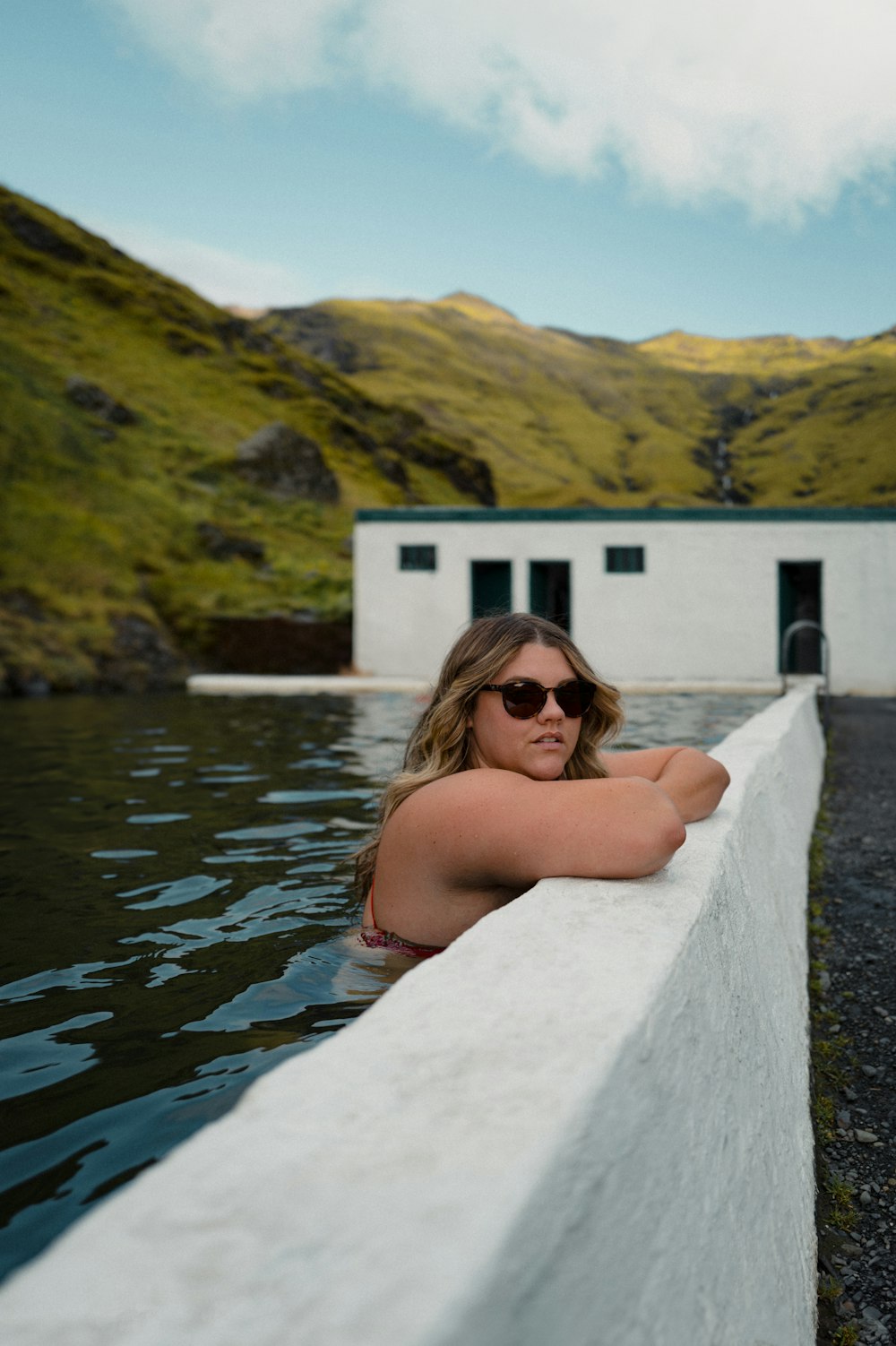 a woman in a bikini sitting on a wall next to a body of water