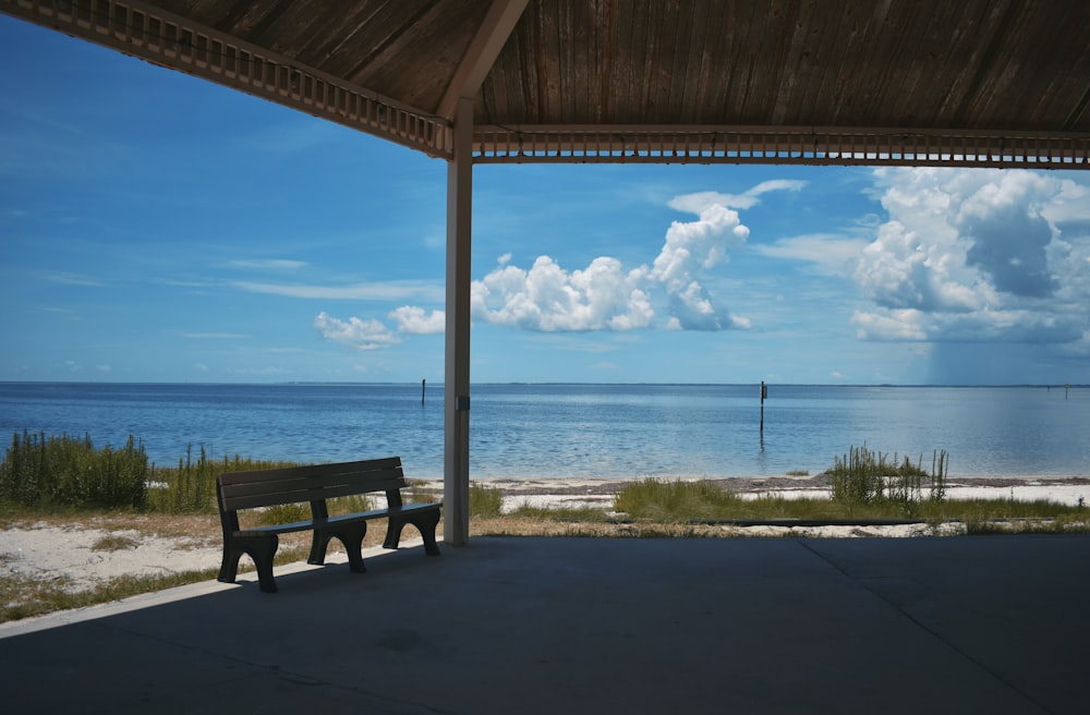 a wooden bench sitting under a roof next to the ocean